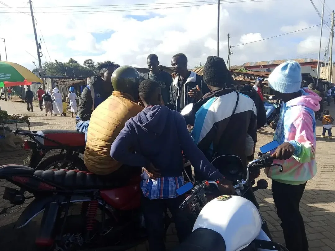 Motorbike riders and residents in conversation on a street in Kabiro